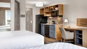 A hotel room with a bed, a desk with a chair, a kitchenette, and a door. - Candlewood Suites Indianapolis Northwest by IHG (Indianapolis)