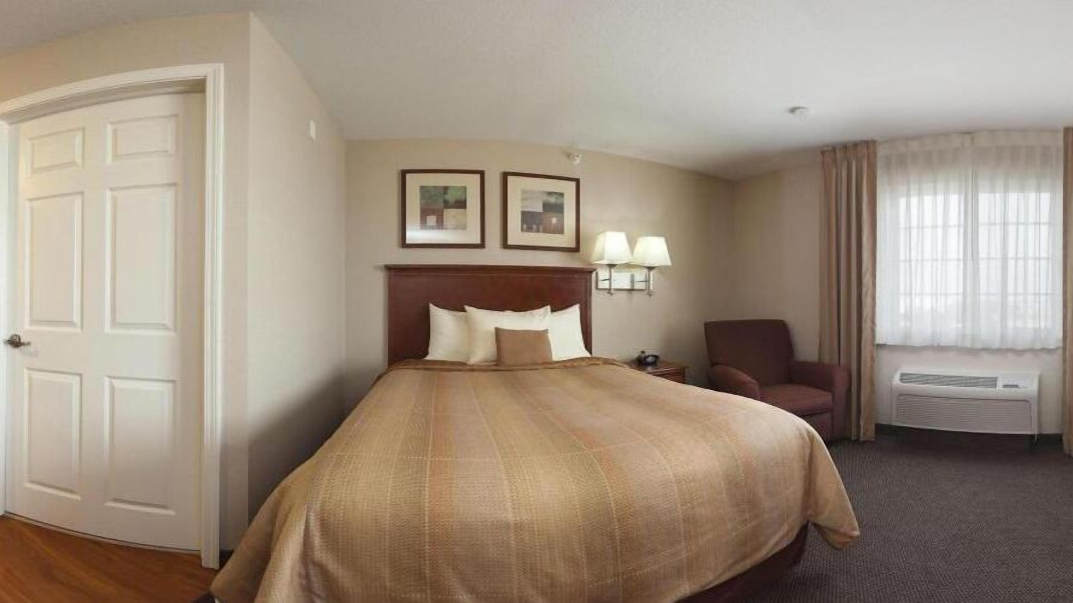 A hotel room with a bed, a chair, a lamp, and a picture frame on the wall.