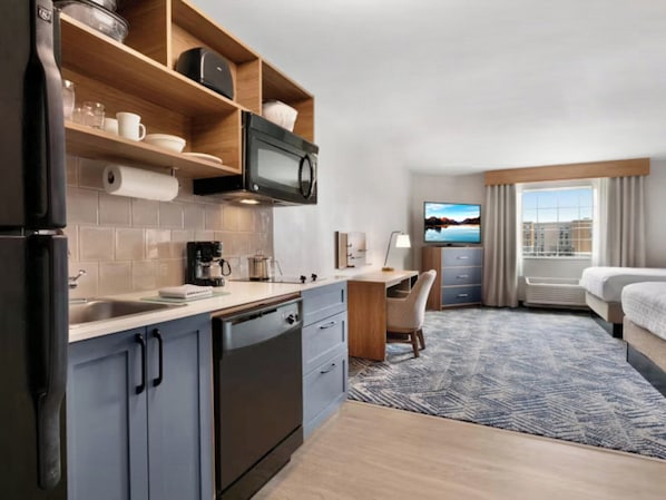 Une chambre d’hôtel équipée d’une kitchenette, d’un lit, d’un bureau et d’une télévision.