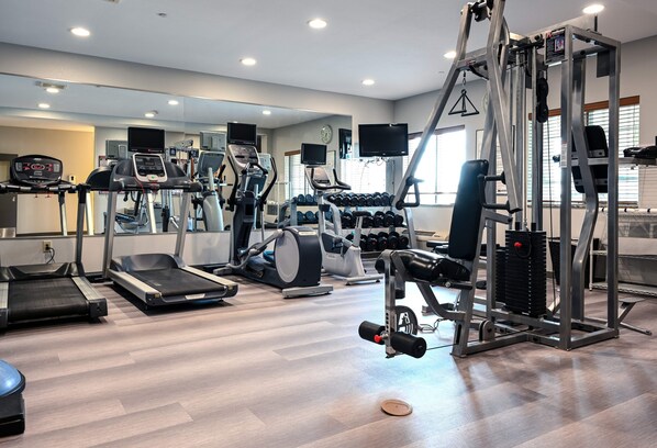 Une salle de sport équipée de tapis de course, de vélos elliptiques, d’un banc de musculation et de poids libres.