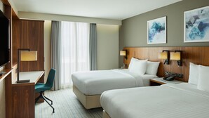 Habitación de hotel con dos camas, un escritorio, una silla, un televisor y obras de arte en la pared.