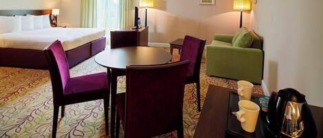Una habitación de hotel con cama, una mesa de comedor con sillas, cafetera y sofá.