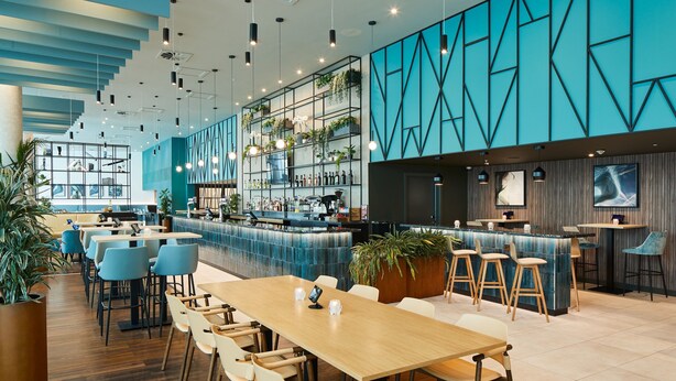 Un restaurante moderno con barra, mesas de madera y diseños geométricos azules en las paredes.