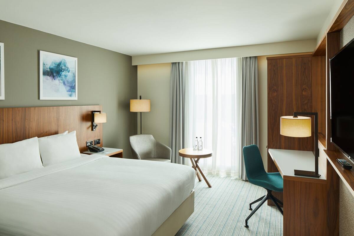 Una habitación de hotel con una cama grande, un escritorio, una silla, un televisor y una ventana con cortinas.
