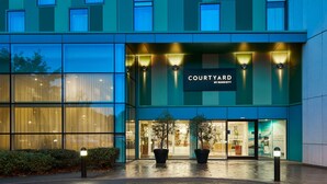 Un hotel Courtyard by Marriott con amplios ventanales de vidrio, un letrero sobre la entrada y plantas en macetas al frente.