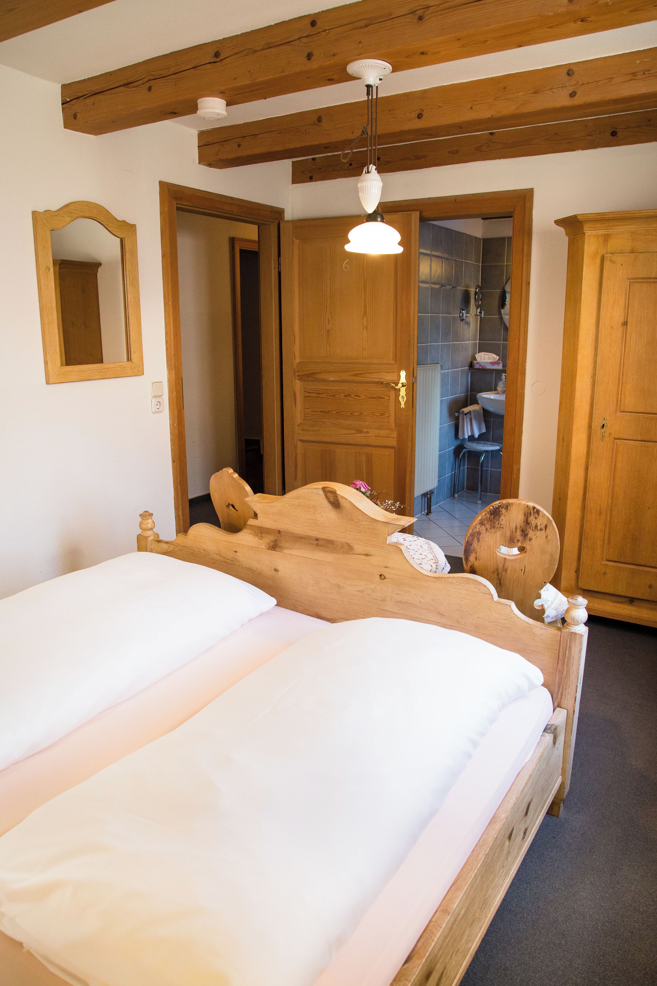 A wooden bed with white bedding in a room with wooden beams and doors.