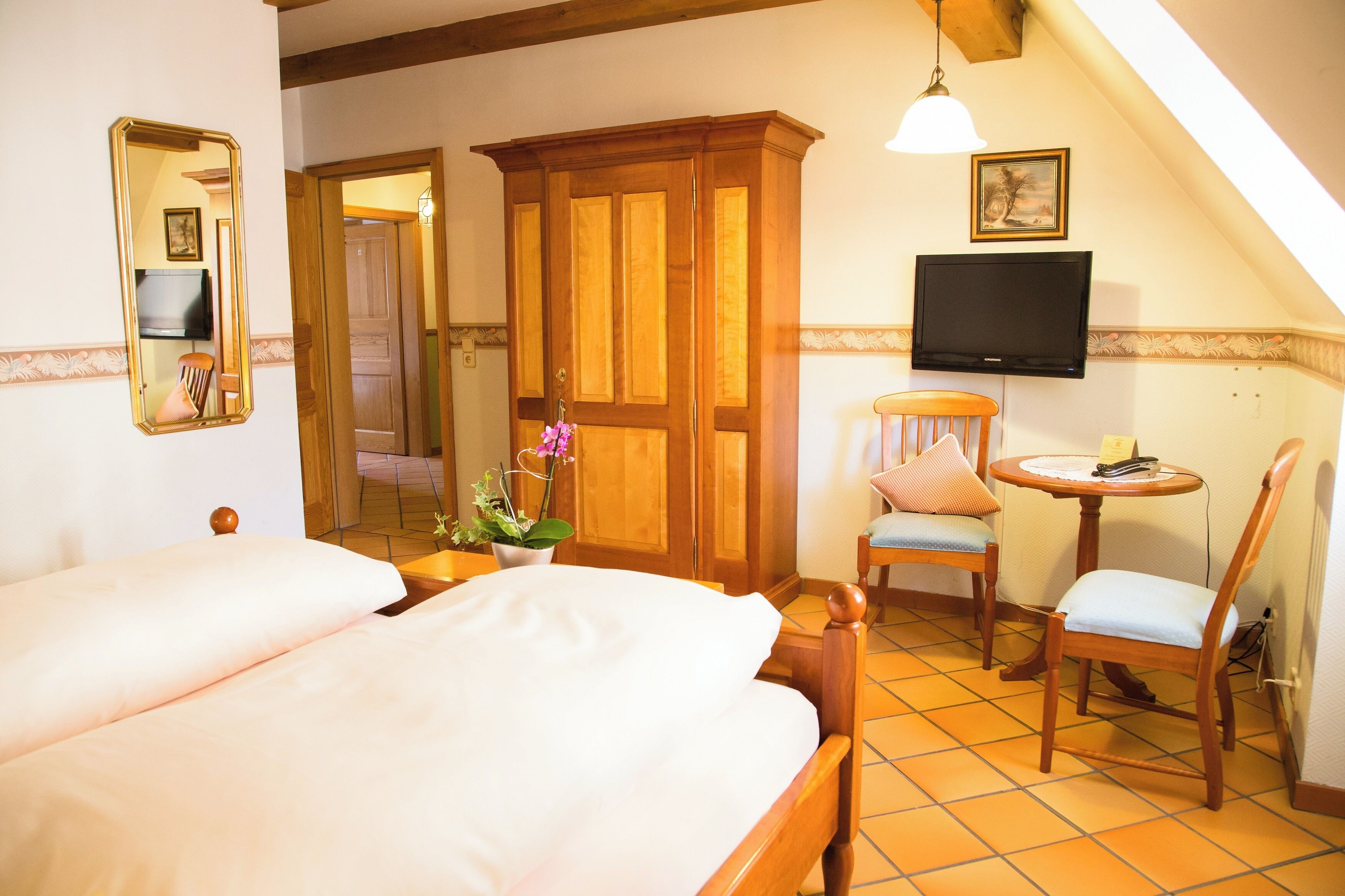 Un dormitorio con cama, un armario de madera, un televisor y una pequeña mesa con una silla.