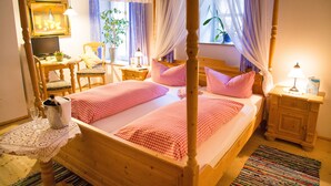 Een hemelbed met vier poten en geruit beddengoed, een nachtkastje met lamp, een stoel, en een tafeltje met een laptop en brillen.