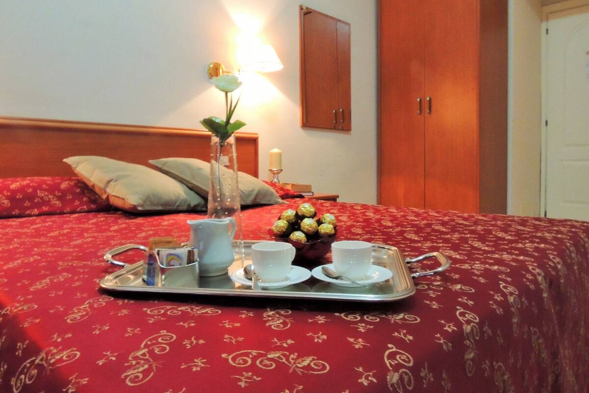A neatly made bed with a tray of breakfast items, a vase with a flower, and a bedside lamp.