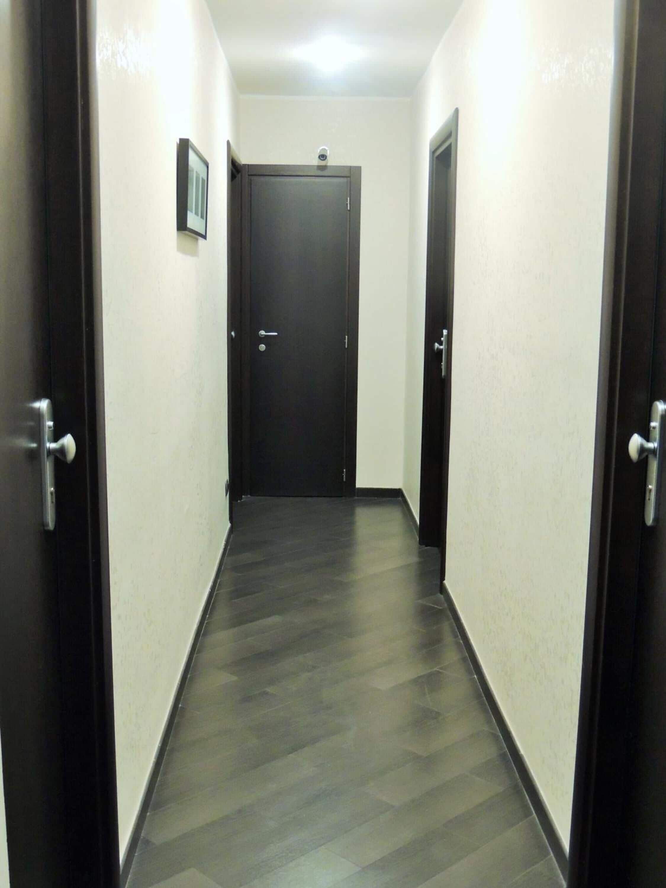 A narrow hallway with dark wooden flooring and white walls.