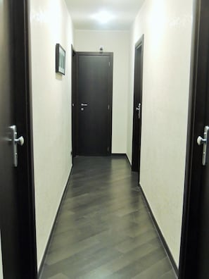 Ein schmaler Flur mit dunklem Holzboden und weißen Wänden.