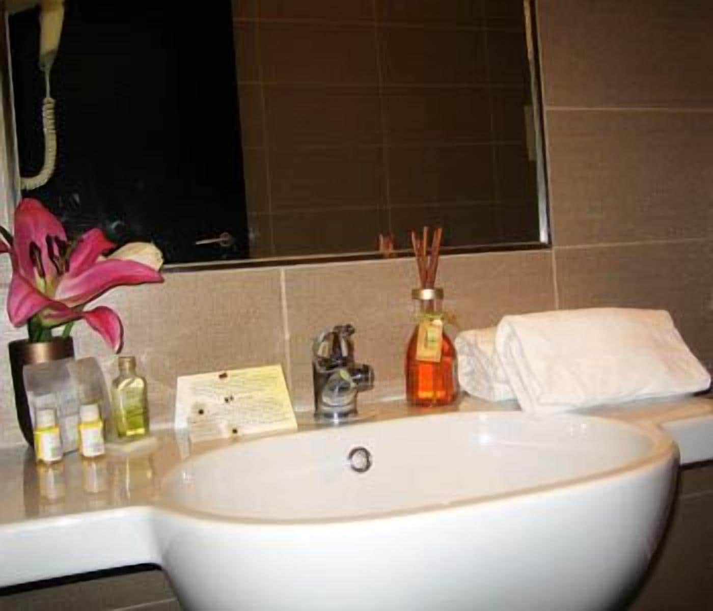 A bathroom with a white sink, a mirror, a towel, and a bottle of perfume.
