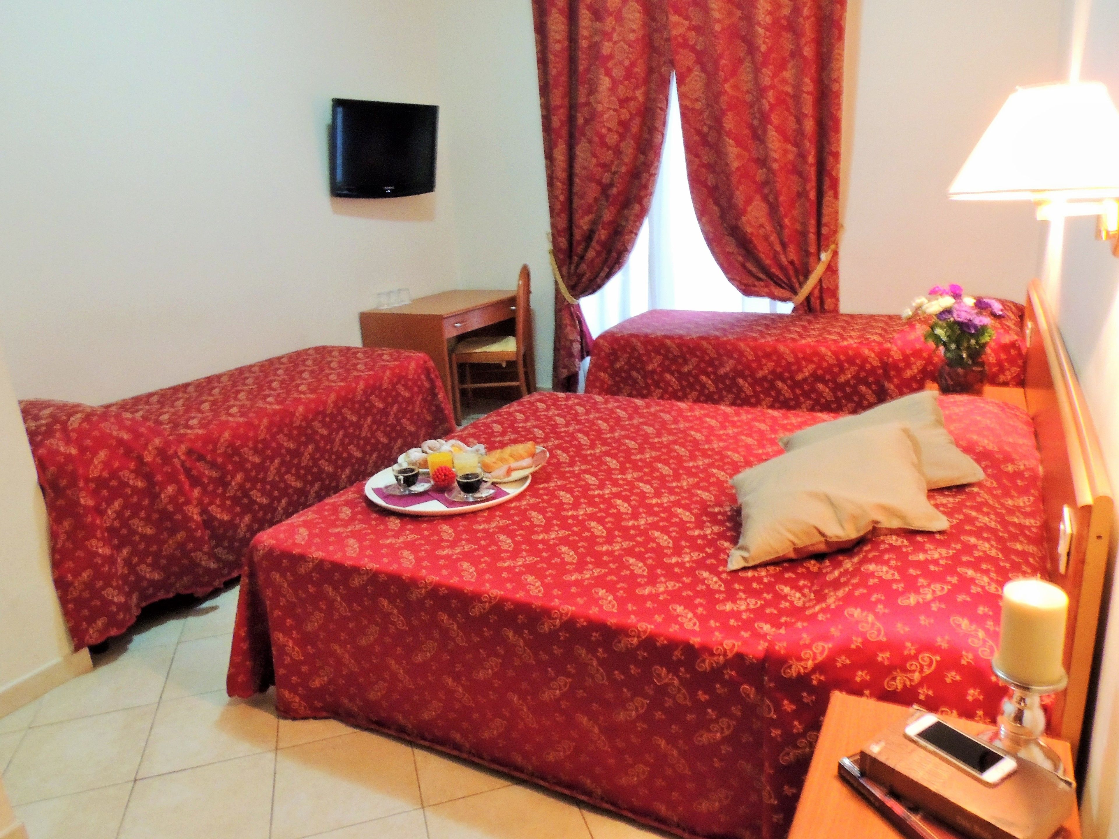 A hotel room with two beds, a desk, a TV, and a bedside table with a phone and a candle.