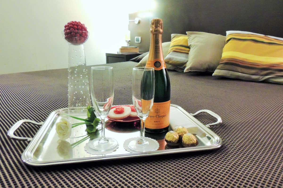 A tray with a bottle of champagne, two glasses, a bowl of cherries, and some pastries on a bed.