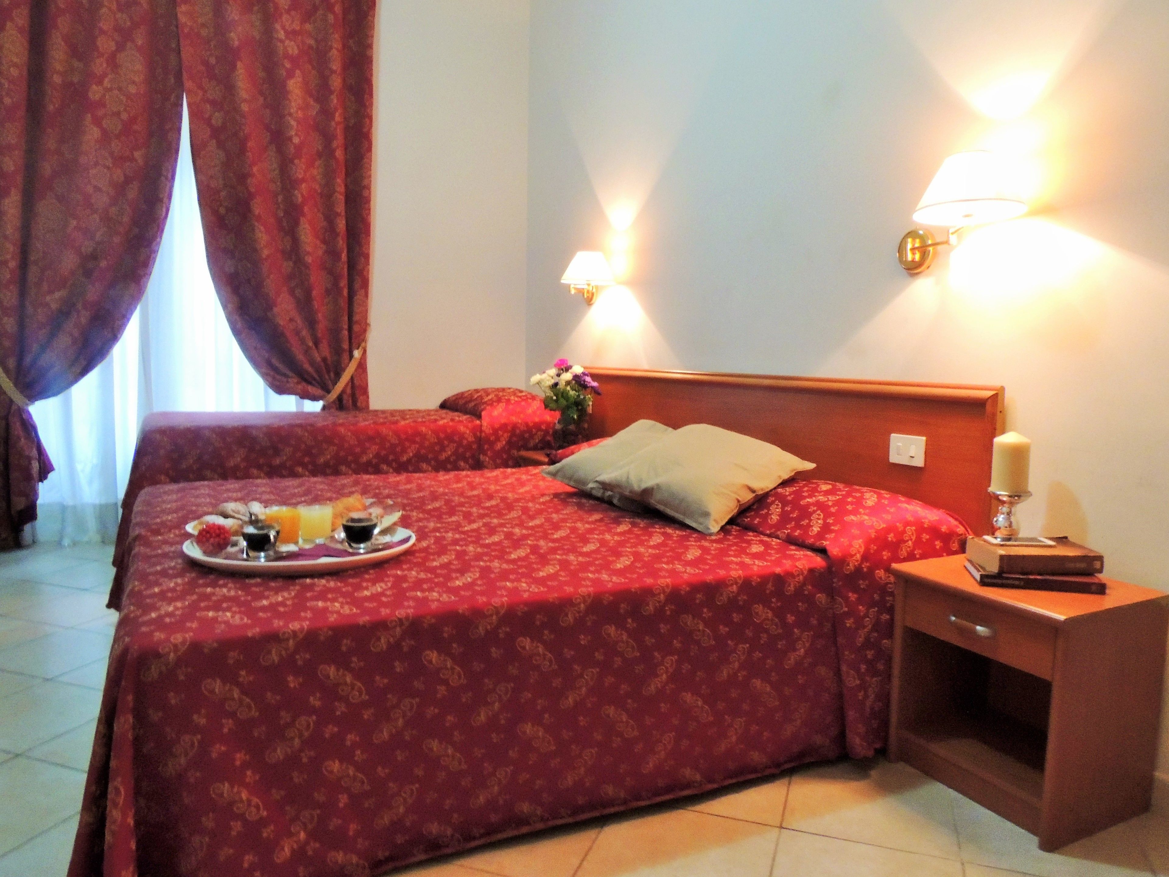A hotel room with two beds, a nightstand, a lamp, and a tray with breakfast items.