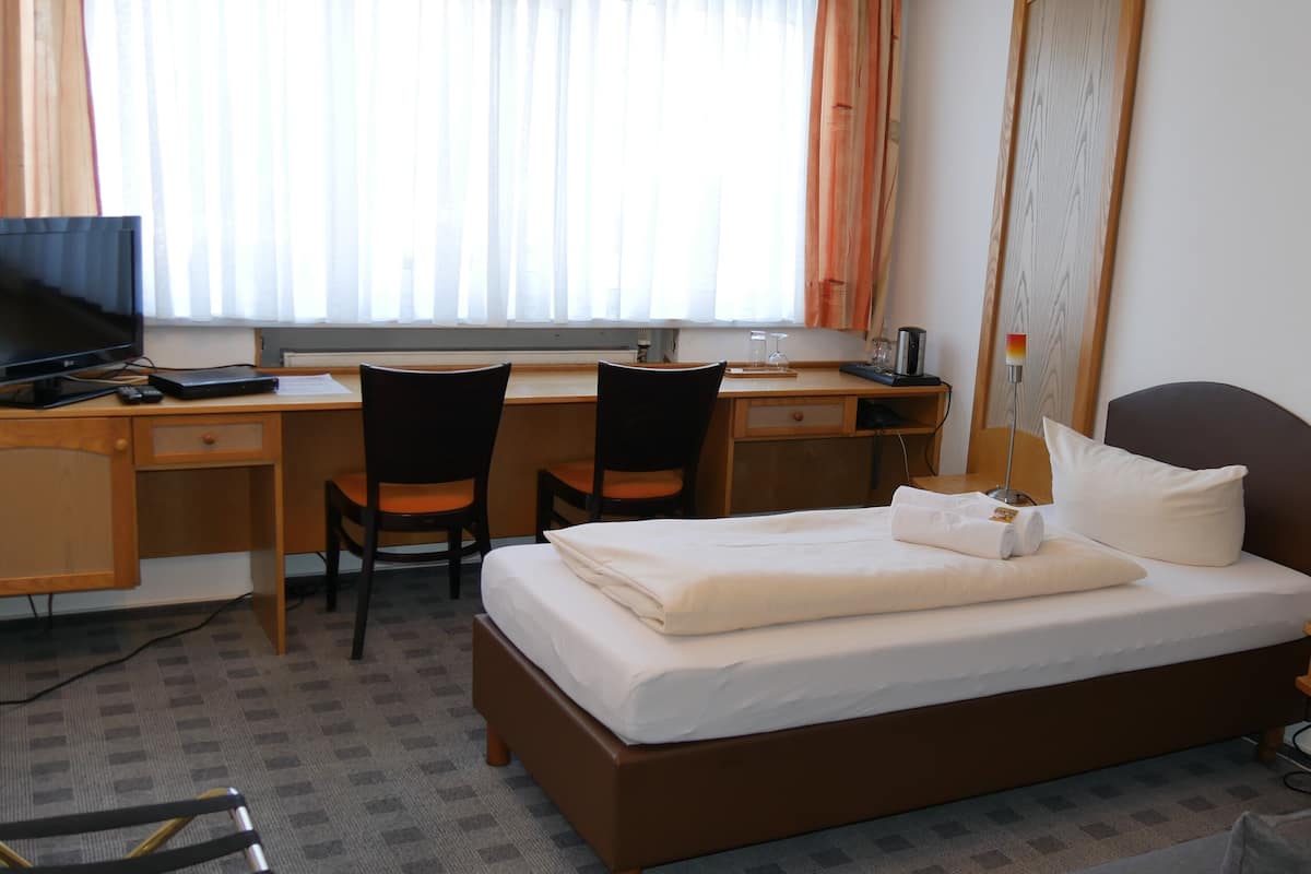 A hotel room with a bed, desk, two chairs, a TV, and a window with curtains.