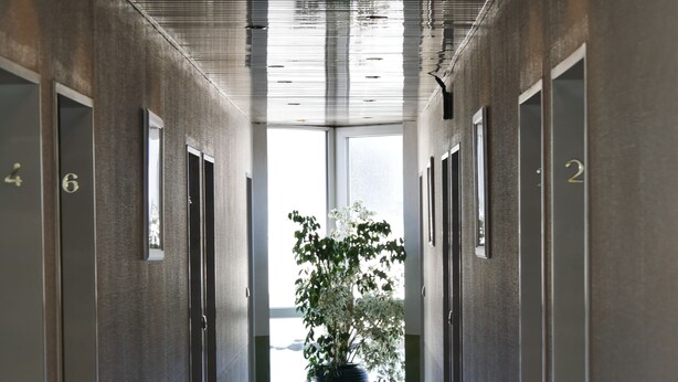 A long, narrow hallway with doors numbered 4 to 6 on the left and 2 on the right, leading to a large window at the end. - Hotel Wasserburg (Munich)