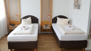 A hotel room with two single beds, wooden headboards, bedside tables with lamps, and a painting on the wall. - Hotel Wasserburg (Munich)