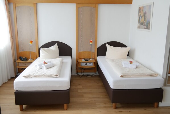 Habitación de hotel con dos camas individuales, cabeceros de madera, mesitas de noche con lámparas y un cuadro en la pared.