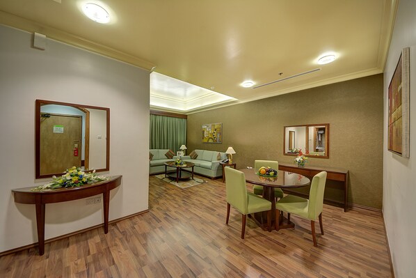 A hotel room with a dining area, a sofa, a coffee table, and a console table with a vase of flowers. - Al Khoory Hotel Apartments (Dubai)
