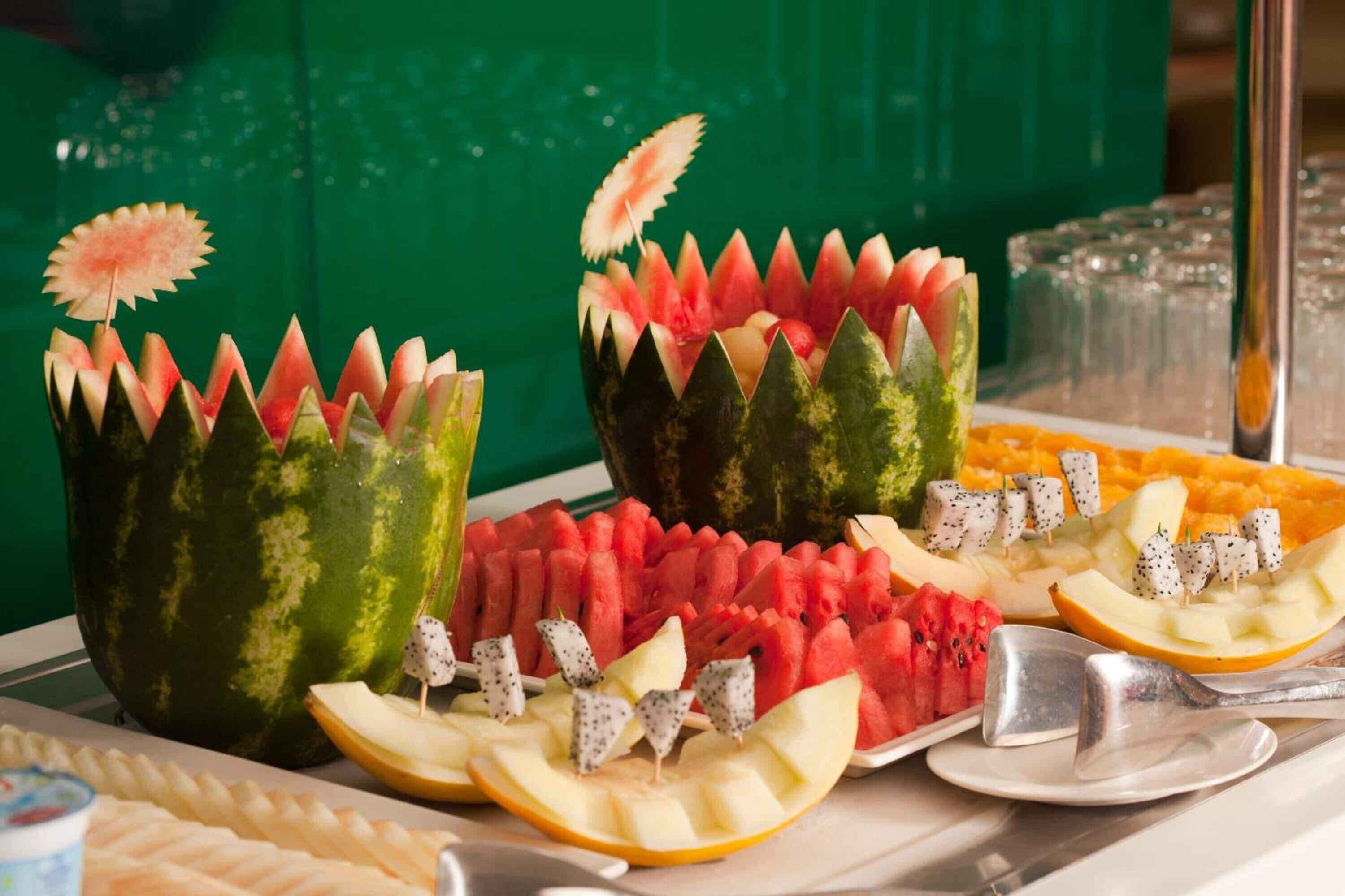A buffet with various fruits and vegetables, including watermelon and apple slices, arranged on a table.