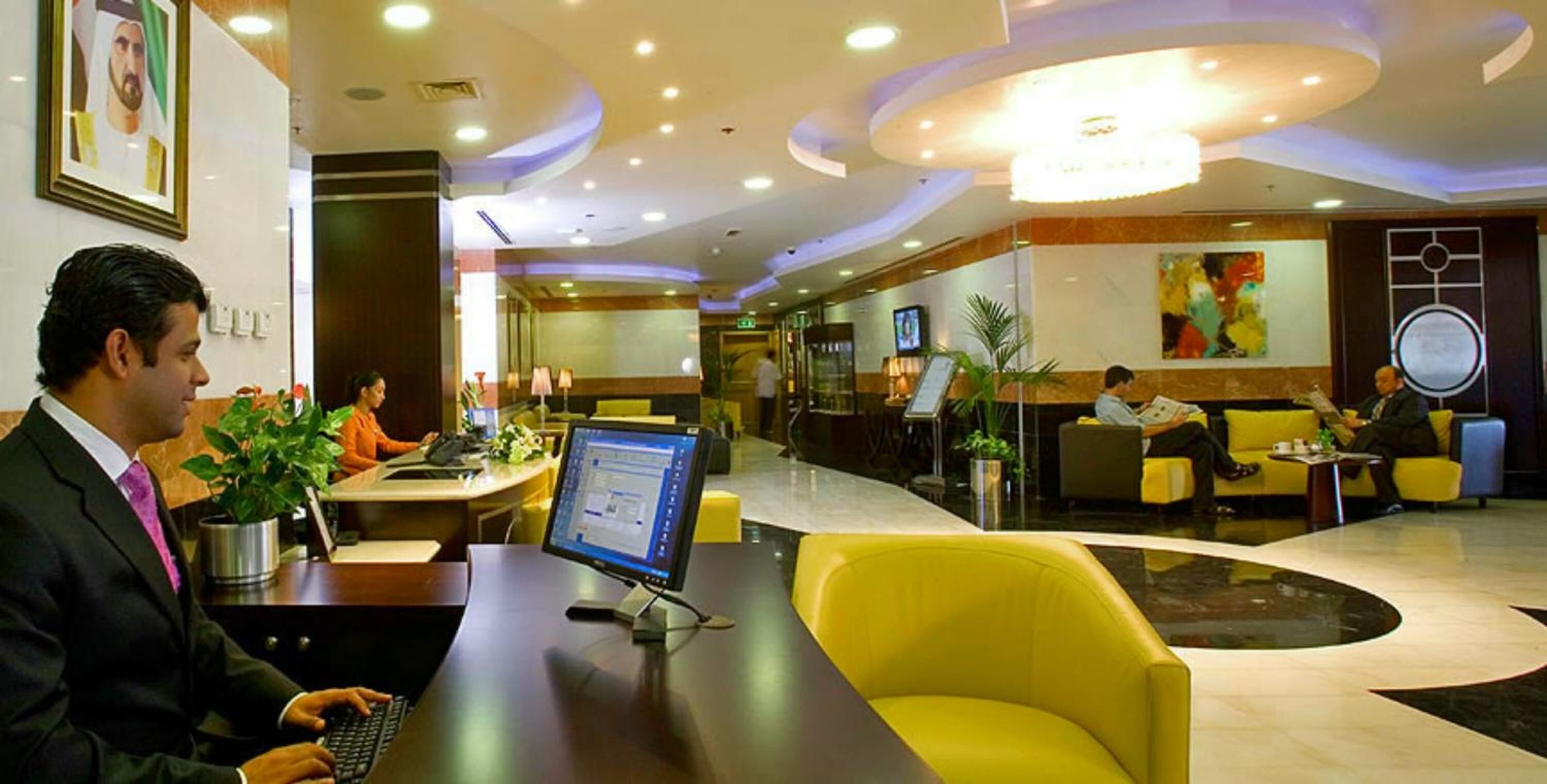 A hotel lobby with a reception desk, yellow seating, and a large chandelier.