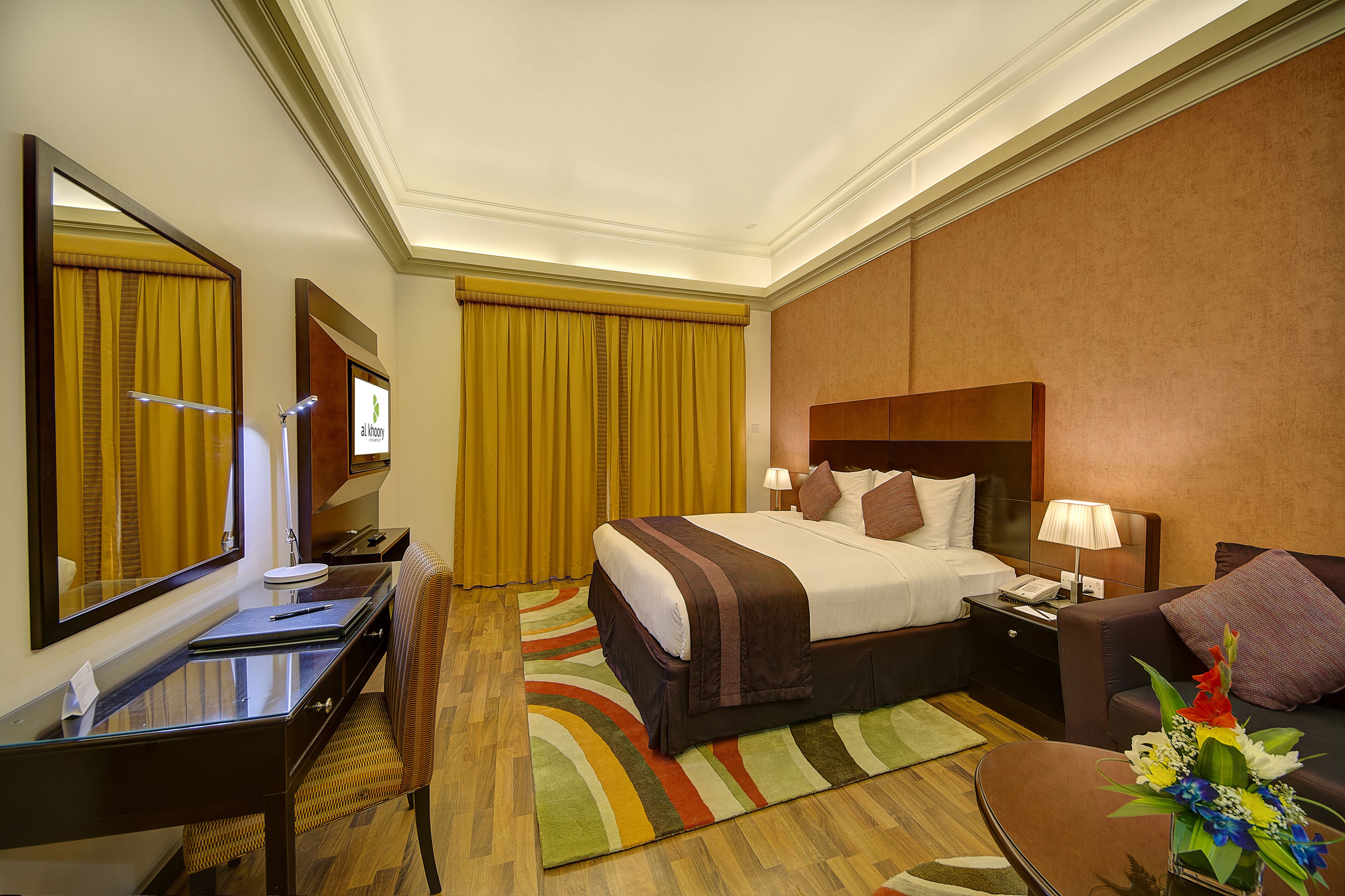 Habitación de hotel con cama, escritorio, silla, mesita de noche, lámpara y un arreglo floral.