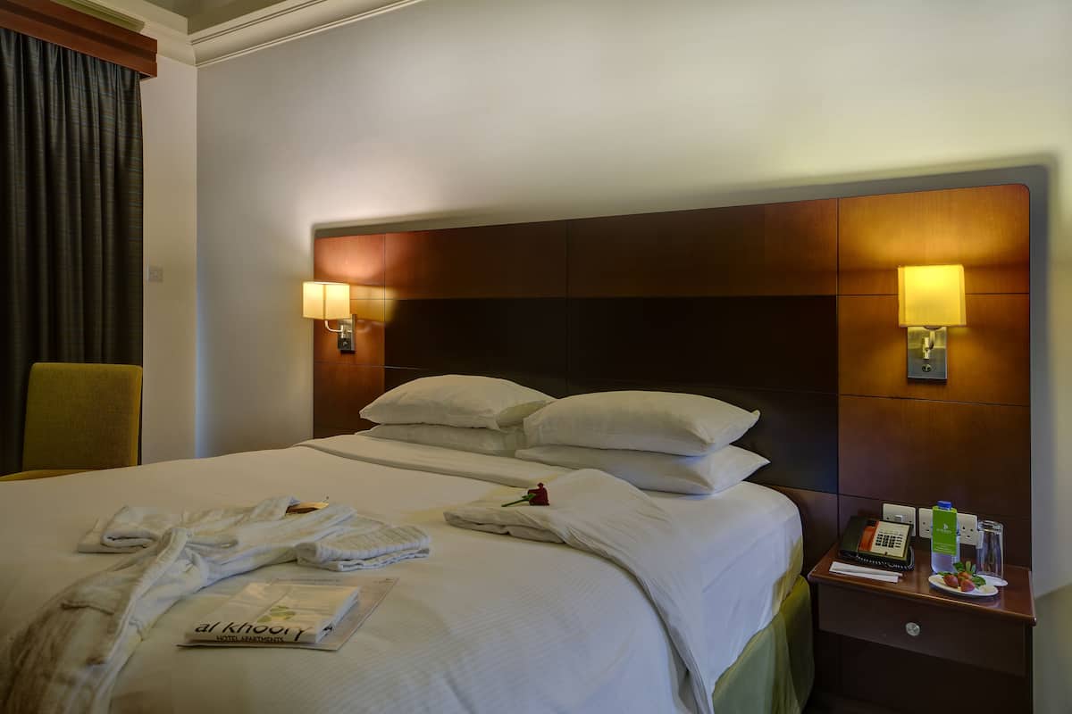 A hotel room with a neatly made bed, a nightstand with a lamp, and a chair.