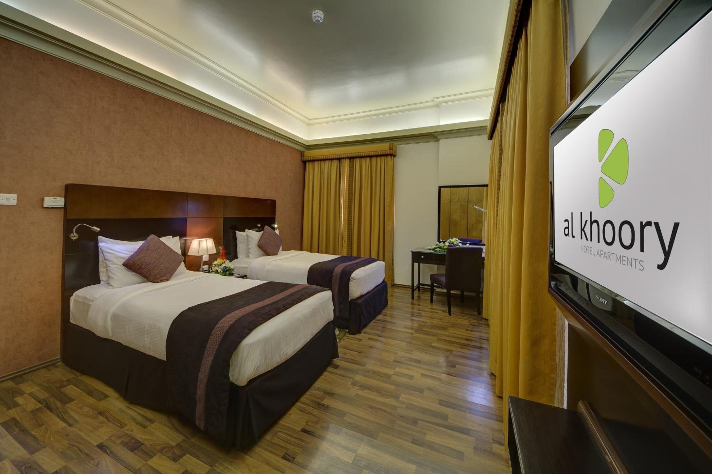 A hotel room with two beds, a desk, a chair, and a television.