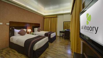 A hotel room with two beds, a desk, a chair, and a television.