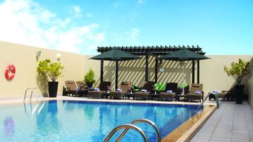 A swimming pool with lounge chairs and umbrellas, surrounded by a tiled deck.