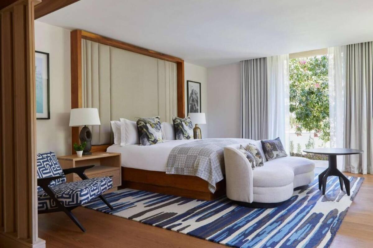 A bedroom with a bed, bedside tables, a chair, a round table, and a view of greenery outside.
