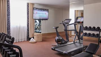 A hotel gym with treadmills, dumbbells, and a TV displaying a tennis match.