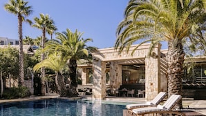 A pool area with lounge chairs, palm trees, and stone architecture.