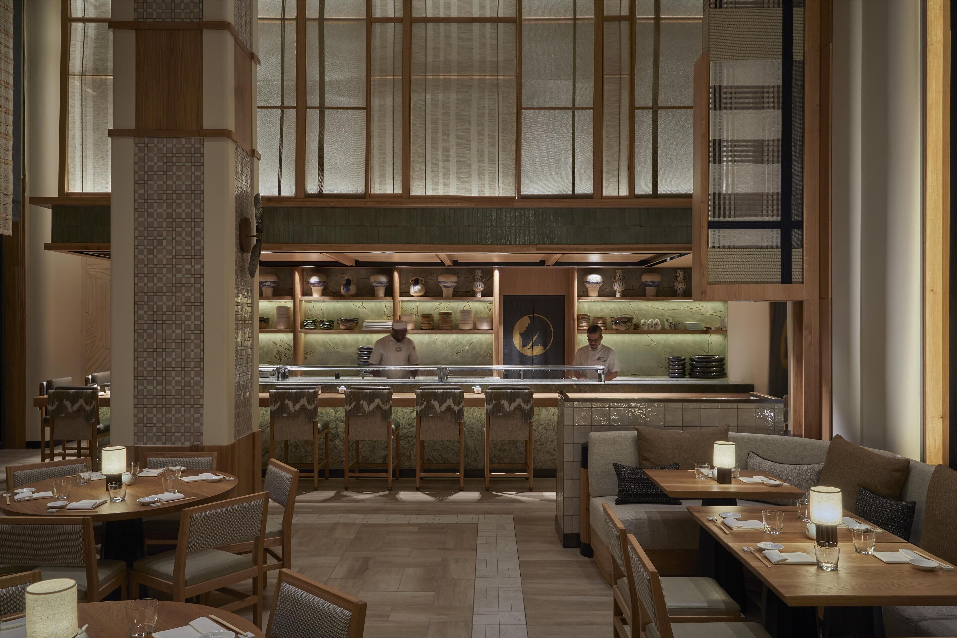 Un restaurante con una decoración tradicional japonesa, que incluye esteras de tatami, mesas bajas y una barra de sushi con chefs.