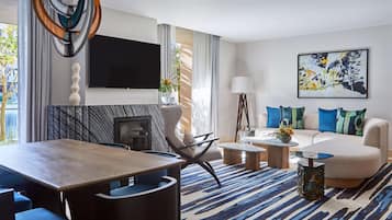 Una sala moderna con comedor, un conjunto de sofá, un televisor de pantalla plana y un cuadro abstracto grande.