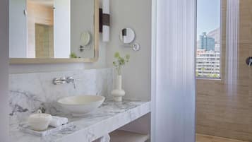 A modern bathroom with a marble sink, a large mirror, a vase with greenery, and a view of a cityscape through a window.