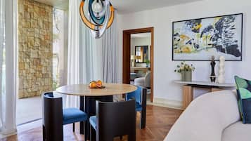 A modern living room with a stone wall, a round wooden table with fruit, blue chairs, a sofa, and a large abstract painting.