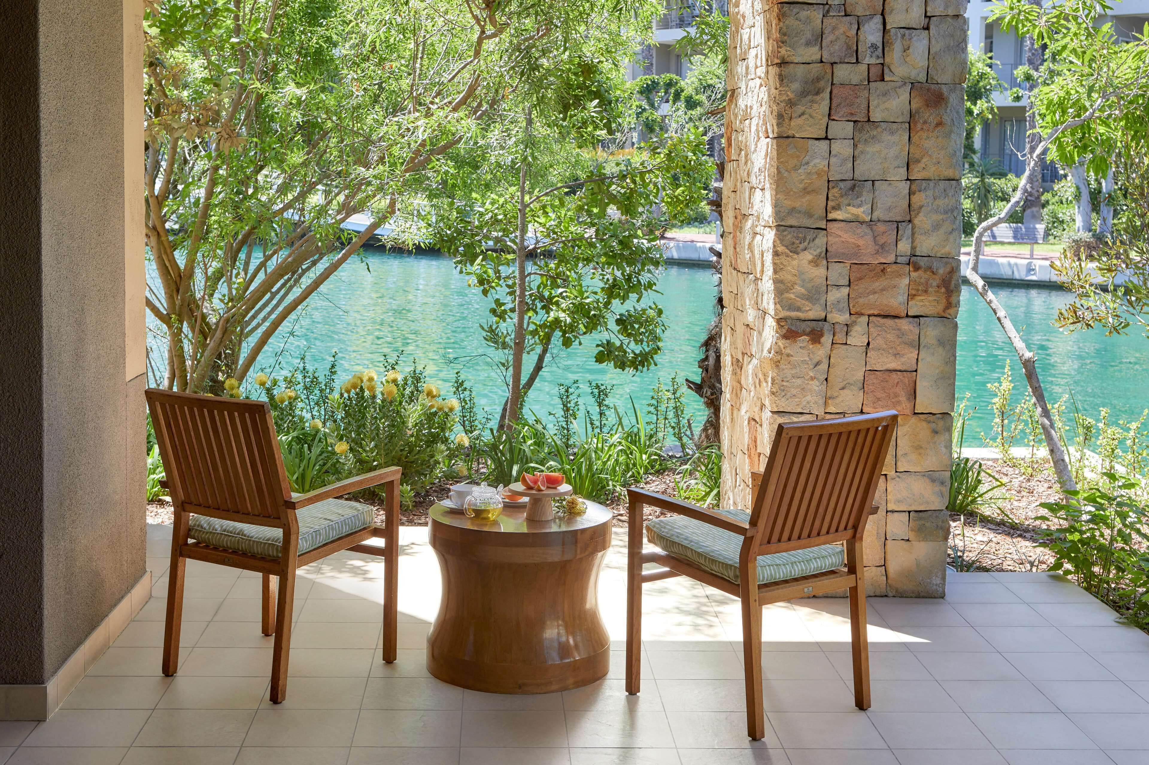 Une terrasse avec deux chaises en bois et une table ronde en bois, donnant sur une étendue d’eau et une zone verdoyante.