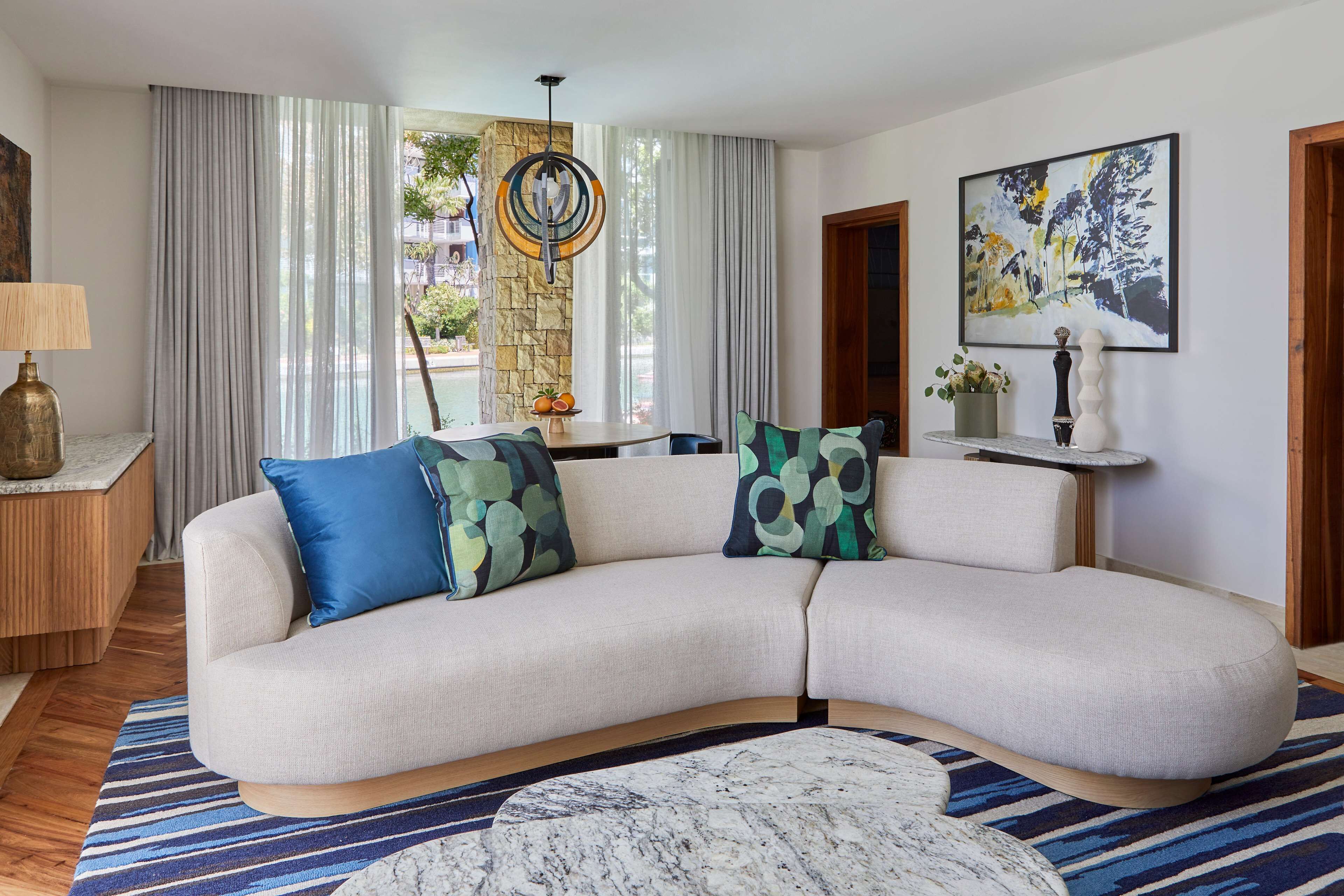 A modern living room with a curved sofa, a marble coffee table, and a large window with curtains.