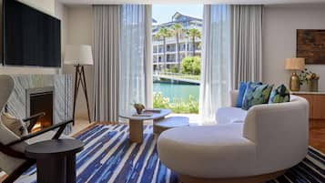 Une chambre d’hôtel moderne dotée d’une grande fenêtre donnant sur un immeuble et sur l’eau. On y trouve un canapé, une petite table et un téléviseur fixé au mur.