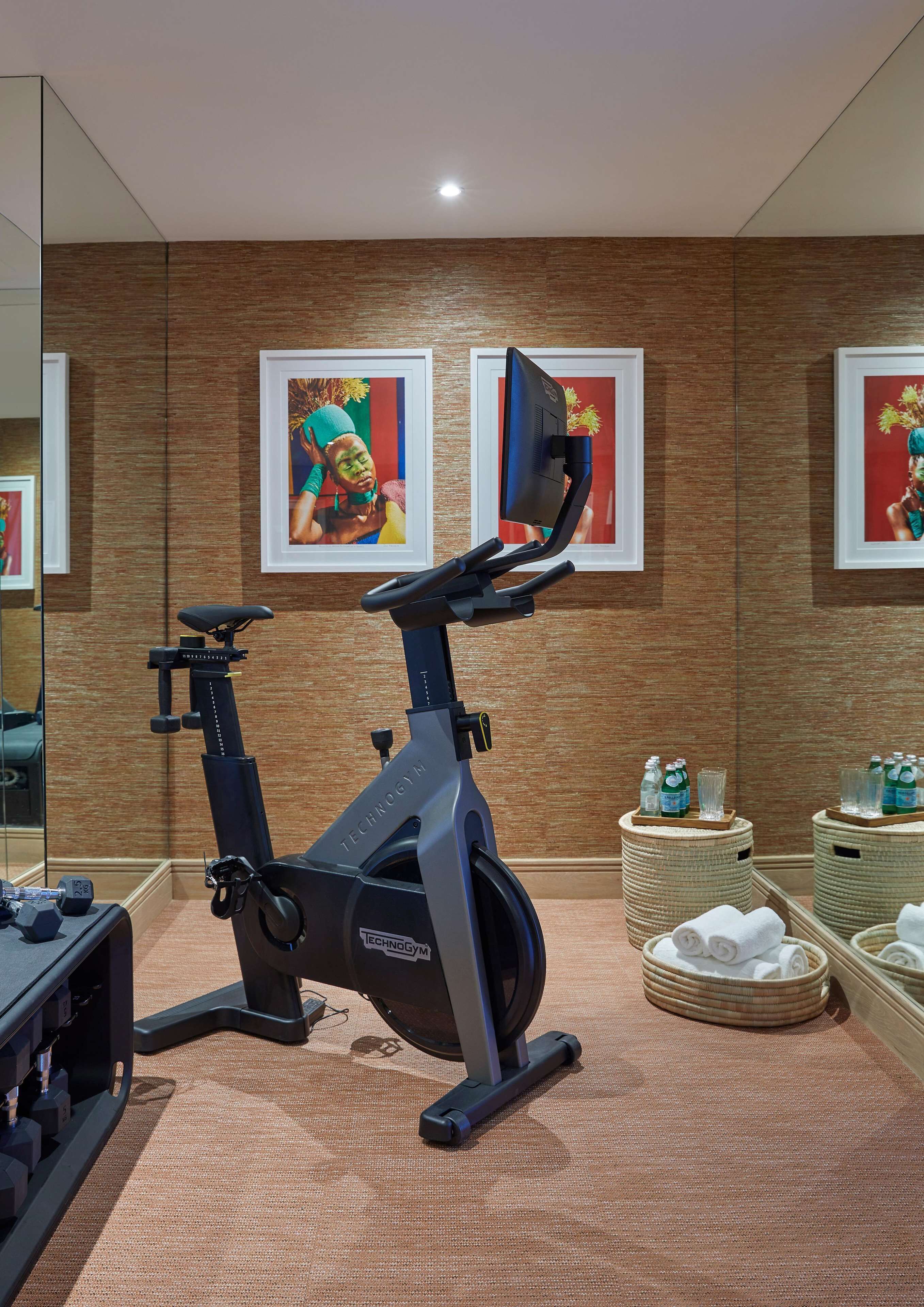 Un gimnasio con bicicletas estáticas, un espejo grande y obras de arte enmarcadas.