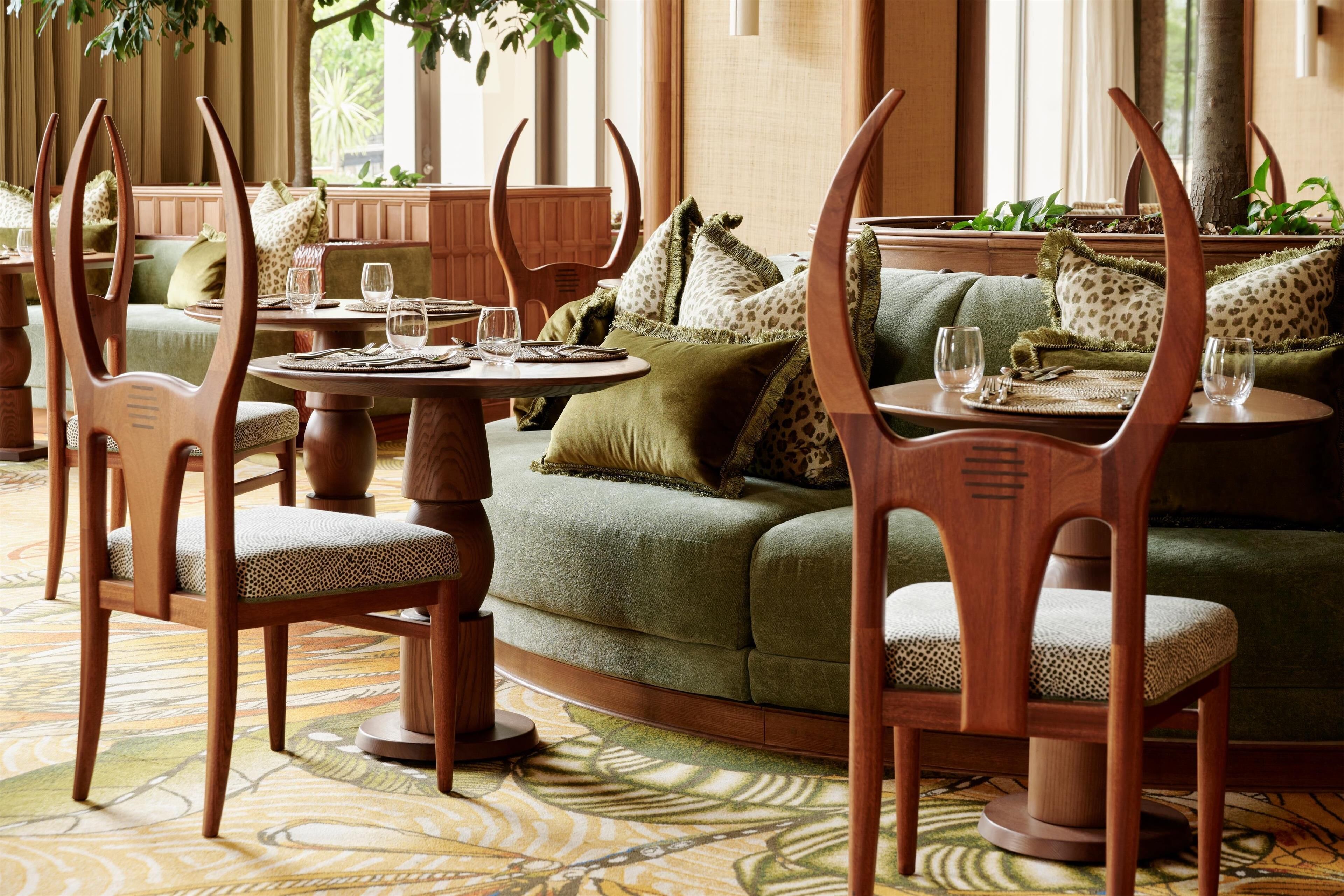 A dining area with wooden chairs and a green sofa, featuring a patterned carpet and natural light from windows.