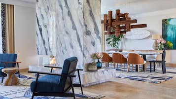 A modern lobby with a marble wall, a wooden sculpture, and a dining area with chairs and a table.