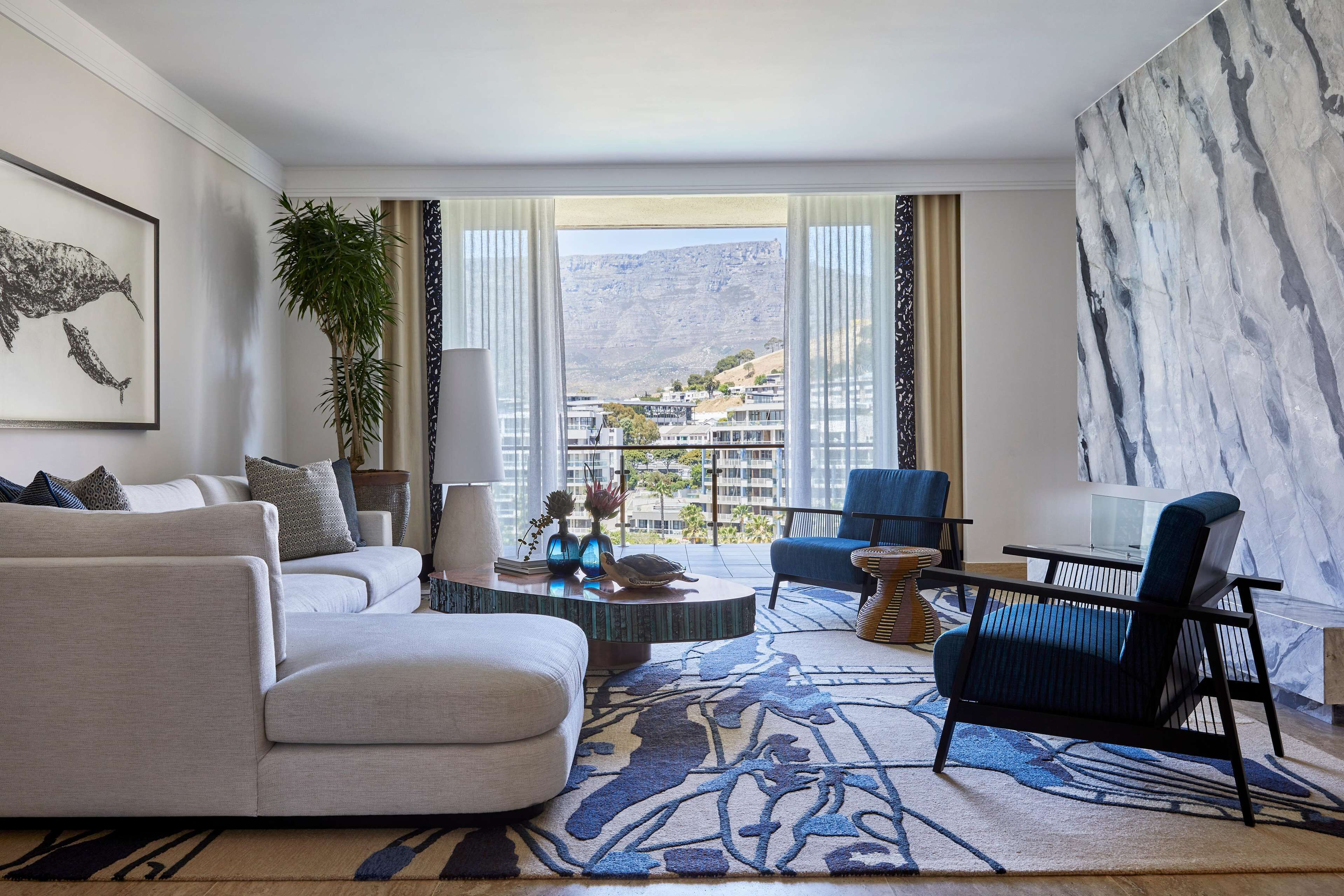 Un salon moderne comprenant un canapé, des fauteuils, une table basse et offrant une vue sur un paysage montagneux grâce à de grandes fenêtres.