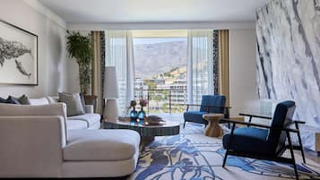 A modern living room with a sofa, armchairs, a coffee table, and a view of a mountainous landscape through large windows.