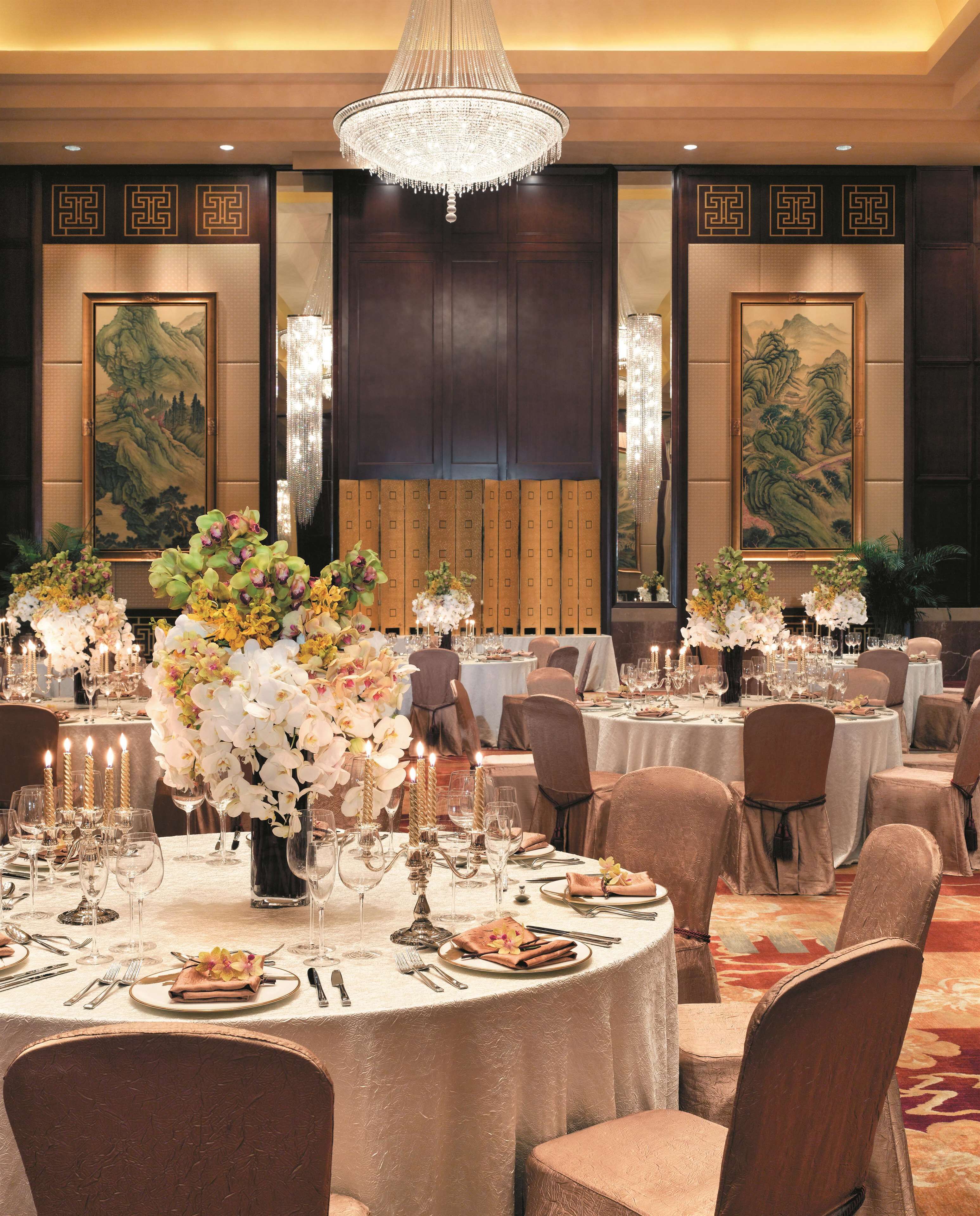 A banquet hall with round tables set for dining, featuring floral centerpieces and candle holders.
