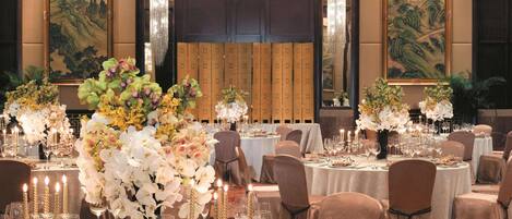 A banquet hall with round tables set for dining, featuring floral centerpieces and candle holders.