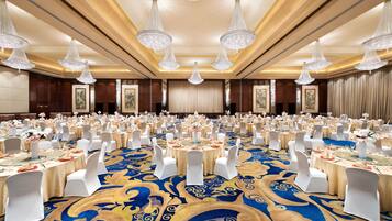 A banquet hall with round tables, white chairs, and chandeliers.