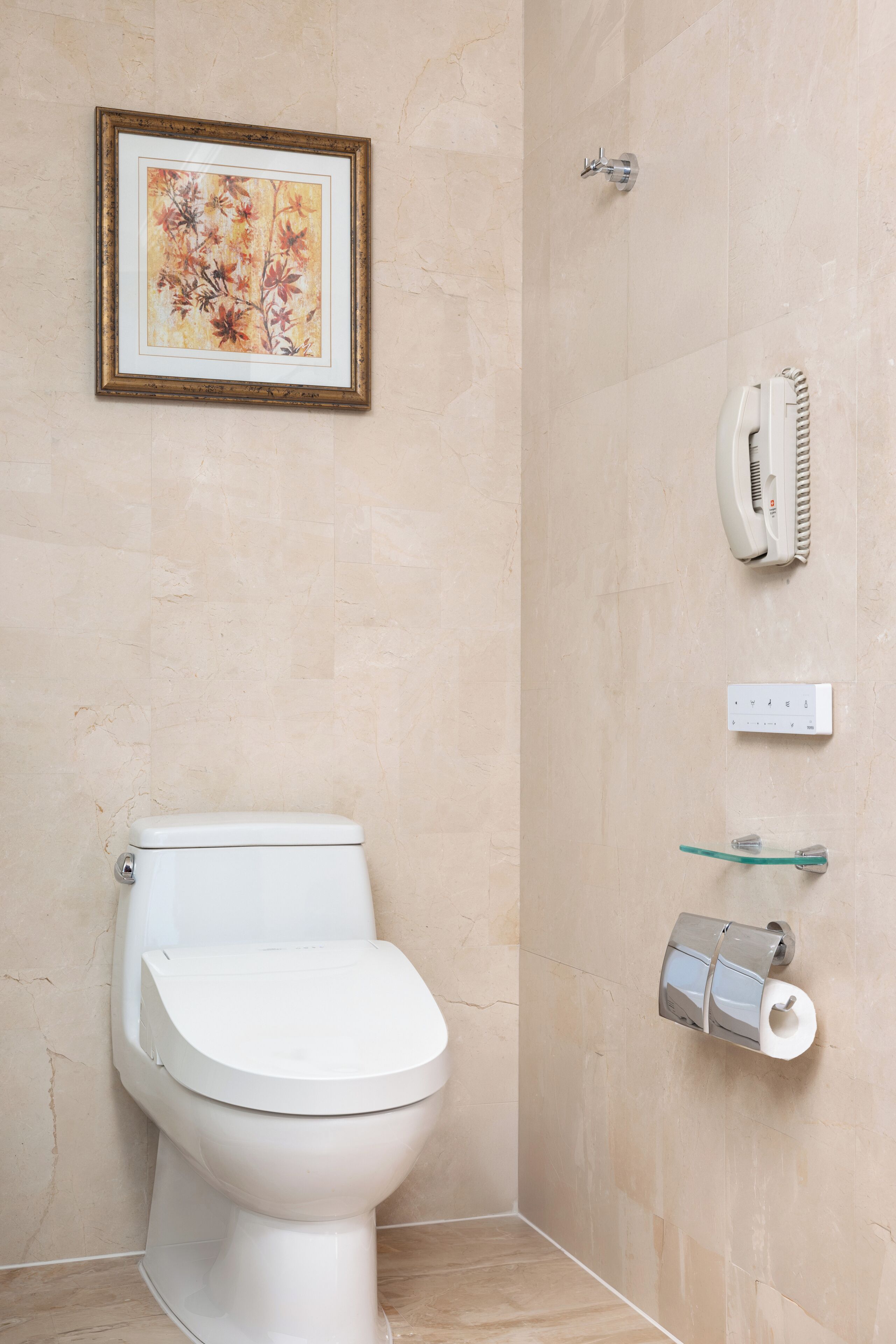 A bathroom with a toilet, a framed floral artwork, a hairdryer, and a toilet paper holder.